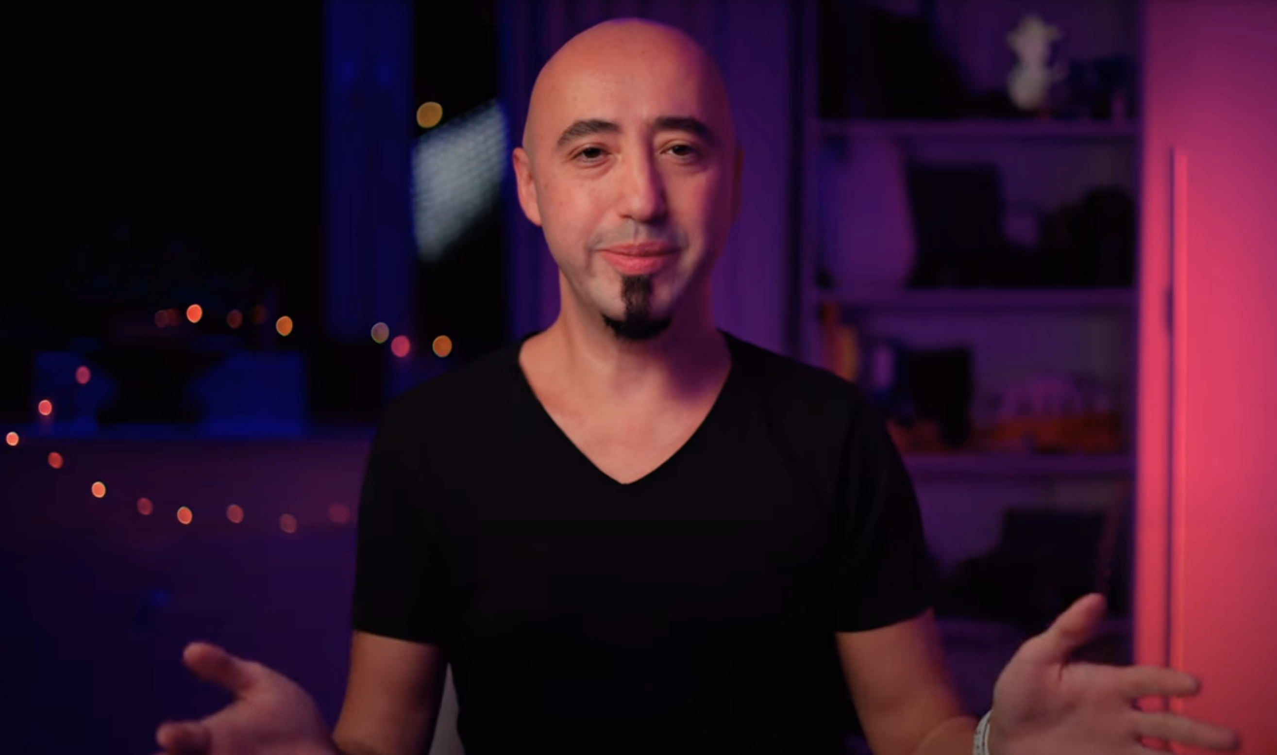 Renkli ışıklı bir odada kameraya gülümseyerek konuşan bir eğitmen.